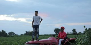 一个印度农民和他的小孩在田里用拖拉机工作