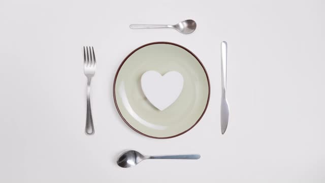 浪漫情人节晚餐创意概念。心形的盘子和银色的佩戴在红色的背景。定格动画。