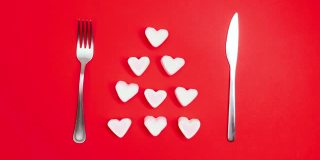 浪漫情人节晚餐创意概念。心形的盘子和银色的佩戴在红色的背景。定格动画。