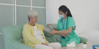 亚洲女护士做血压测量资深妇女病人在客厅在家。家庭医疗保健的概念。