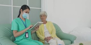 亚洲护士在家客厅用平板电脑对老年患者进行咨询和跟踪护理，在进行家庭保健时在家与医生进行健康咨询和医疗报告。