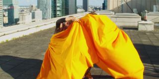身穿迷彩服的女舞者在屋顶上表演。躲在橙色的织物后面