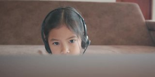 亚洲女童学生戴上耳机，通过视频电话与老师在线学习。由于Covid - 19大流行，在隔离期间，孩子正在用笔记本电脑在家学习。