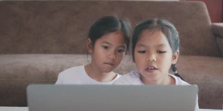 两名亚洲女童学生通过视频一起与老师在线学习。由于Covid - 19大流行，兄弟姐妹在隔离期间用电脑在家学习。