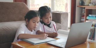 两名亚洲女童学生通过视频一起与老师在线学习。由于Covid - 19大流行，兄弟姐妹在隔离期间用电脑在家学习。
