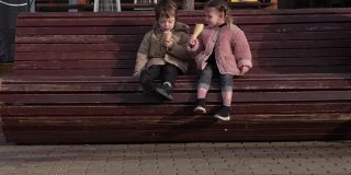 小男孩和小女孩在长凳上吃甜筒冰淇淋