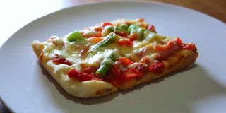 女人拿起一块自制的披萨，配上蔬菜，火腿和奶酪放在白色的盘子里。最好的意大利美食。最喜欢的食物。隔离期间做饭。