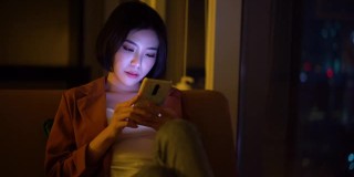 美丽的亚洲女人在晚上使用智能手机