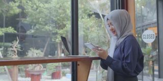快乐多元的亚洲穆斯林年轻女子坐在café桌喝咖啡