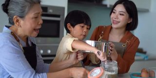 年轻的亚洲男孩在家里与母亲和祖母学习烘焙