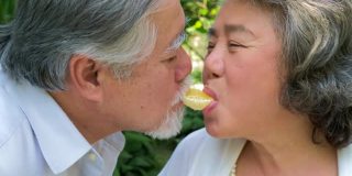 快乐的亚洲老年夫妇微笑着健康的橘子水果，老年男女退休后有一个幸福的生活，人们的生活理念。