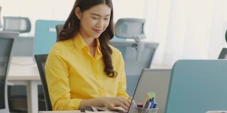 幸福迷人的亚洲女人在现代办公室或联合办公空间的商业创业的想法和要求，黄色衬衫与电脑笔记本电脑工作，创业概念