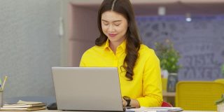 幸福迷人的亚洲女人在现代办公室或联合办公空间的商业创业的想法和要求，黄色衬衫与电脑笔记本电脑工作，创业概念