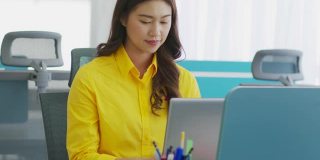 商务亚洲女人在黄色衬衫会议通过VDO会议展示销售报告，并解释在现代办公室或联合办公空间创业