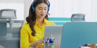 快乐年轻的亚洲商务女性戴着耳机与她的业务团队在现代办公室或联合办公空间进行在线视频电话会议，创业概念