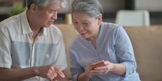 亚洲华人老年夫妇在周末休闲时间在客厅学习使用智能手机