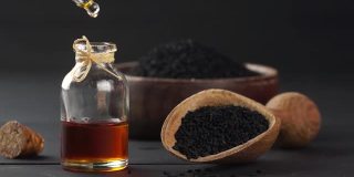 玻璃瓶中的黑色孜然籽精油，在黑色木质背景下舀取黑豆，油滴