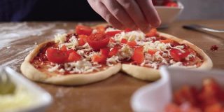 近-美味的意大利披萨，马苏里拉奶酪和香蒜沙司。厨师把美味的樱桃番茄切片。烹饪过程