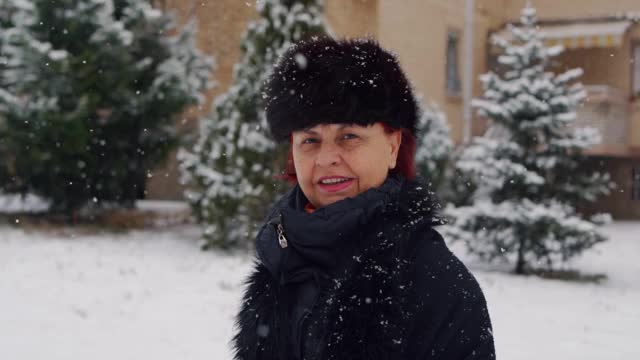 美丽的高级女人戴着冬天的帽子和花时间在户外而下雪