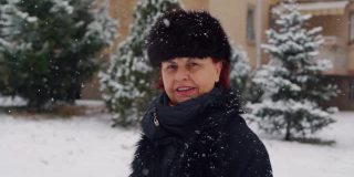美丽的高级女人戴着冬天的帽子和花时间在户外而下雪