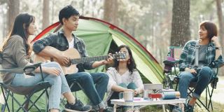 一群朋友在露营旅行中坐在帐篷外面弹吉他