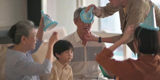 亚洲华人男子帮助他的父亲戴上派对帽，准备在家里的客厅庆祝生日