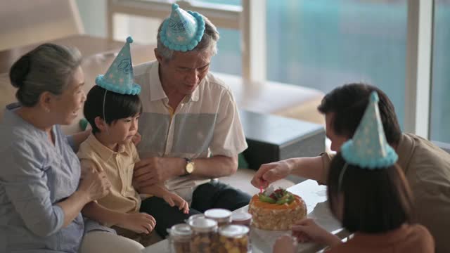亚洲华人多代同堂在客厅拍手，唱生日歌庆祝6岁男孩的生日