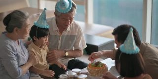 亚洲华人多代同堂在客厅拍手，唱生日歌庆祝6岁男孩的生日