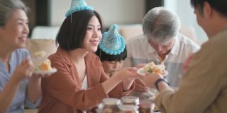 亚洲华人多代同堂庆祝生日，孙子戴着派对帽在客厅吃生日蛋糕