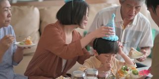 亚洲华人多代同堂庆祝生日，孙子戴着派对帽在客厅吃生日蛋糕