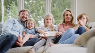 一家人坐在家里的沙发上笑着看电视和爆米花视频素材模板下载