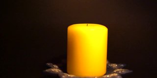 在一片漆黑中，人们用燃烧的火柴点燃一支黄色的节日蜡烛。手在框架里。