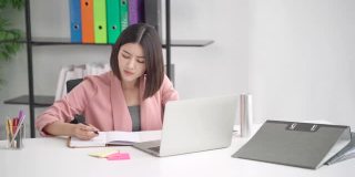 专注专注的亚洲女商人专业工作者写笔记规划思维创意创意策略，员工努力工作在现代办公室使用笔记本电脑技术