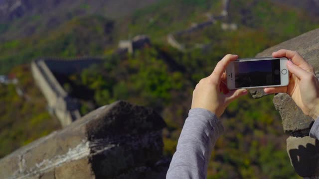 2018年10月29日，中国北京:一名女子用手机拍摄中国长城的慢动作照片，长城在山的一侧开始倒塌
