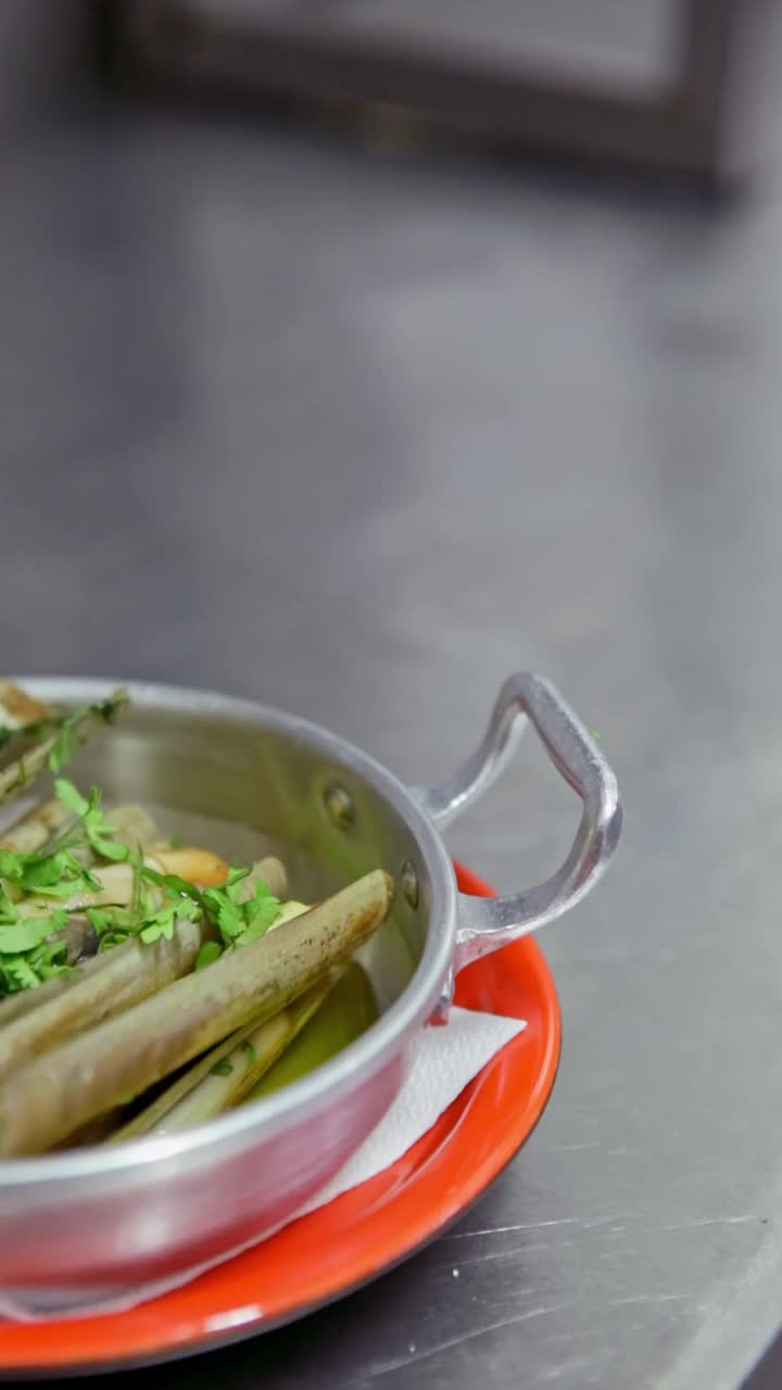 开胃的蛤蜊配上大蒜、香草，放在一个铝制的盘子里，再点缀上一打柠檬。垂直视频。特写镜头。