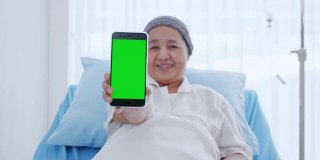 一位身患癌症的老年妇女坐在床上，正在用她的智能手机显示一些信息。