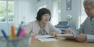 迷人的年轻老年亚洲公民夫妇坐在家里的书桌桌上的水彩画艺术品感觉快乐的心理健康治疗或亚洲老年人隔离活动的生活理念。