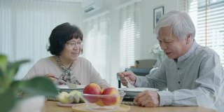 迷人的年轻老年亚洲公民夫妇愉快地坐着聊天，吃汤的健康营养早餐餐在餐桌上的早上在老亚洲人的观念日常生活方式。