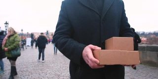 穿黑色外套的快递员拿着装着包裹的纸板箱。