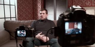 男博主接受采访时坐在沙发前摄像机前回答记者提问
