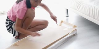 亚洲女孩使用切割机打开棕色盒子，这是从网上购物买的一些家具，生活方式的概念。