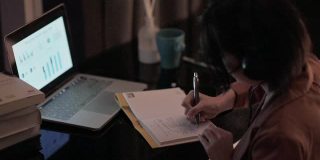 亚洲华人美丽的女人使用笔记本电脑工作，在家自习室书写耳机