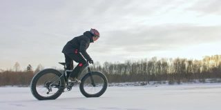 职业极限运动爱好者在户外骑着胖胖的自行车。冬天，骑自行车的人在冰雪上骑车。男人在山地车上表演特技戴着头盔和眼镜，轮胎很大。慢镜头180 fps。