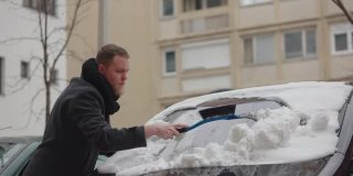 在他去工作之前，年轻人用塑料扫把和刮冰器清理他的车
