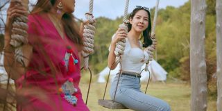 年轻有魅力的亚洲女性朋友女性一起享受休闲放松周末假期玩秋千在游乐场公园的旅游概念