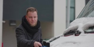 在用刨冰器清理车上积雪时，一名男子向手中吹气，这样他就能保持温暖