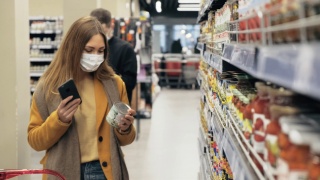 超市里，一名妇女戴着医用口罩扫描商品上的条形码视频素材模板下载