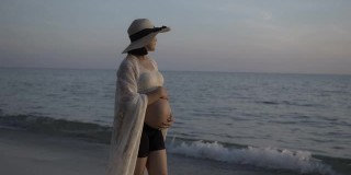 一名孕妇在沙滩上散步时抚摸着自己的肚子。