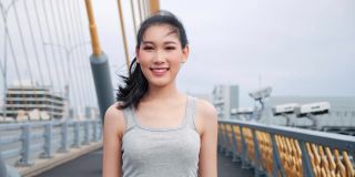 美丽的亚洲女人看着镜头微笑迷人优雅的亚洲女士在高速公路大桥街道城市的运动胸罩肖像。4 k慢动作。