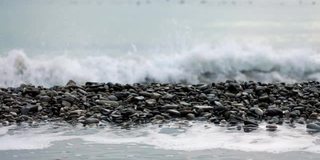 海浪拍打在卵石滩上。镜头的焦点从海岸转移到地平线，那里有一群鸟在游泳。缓慢的运动。冬季